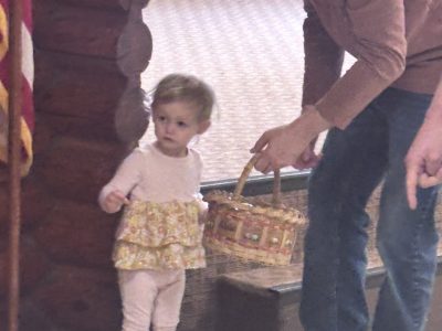 Dad holds an easter egg basket while his young daughter stares at the Easter Bunny